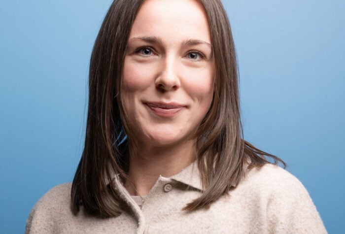 A picture of Holly Welch. A woman in her 30s with straight brown hair and brown eyes, wearing a brown jumper.