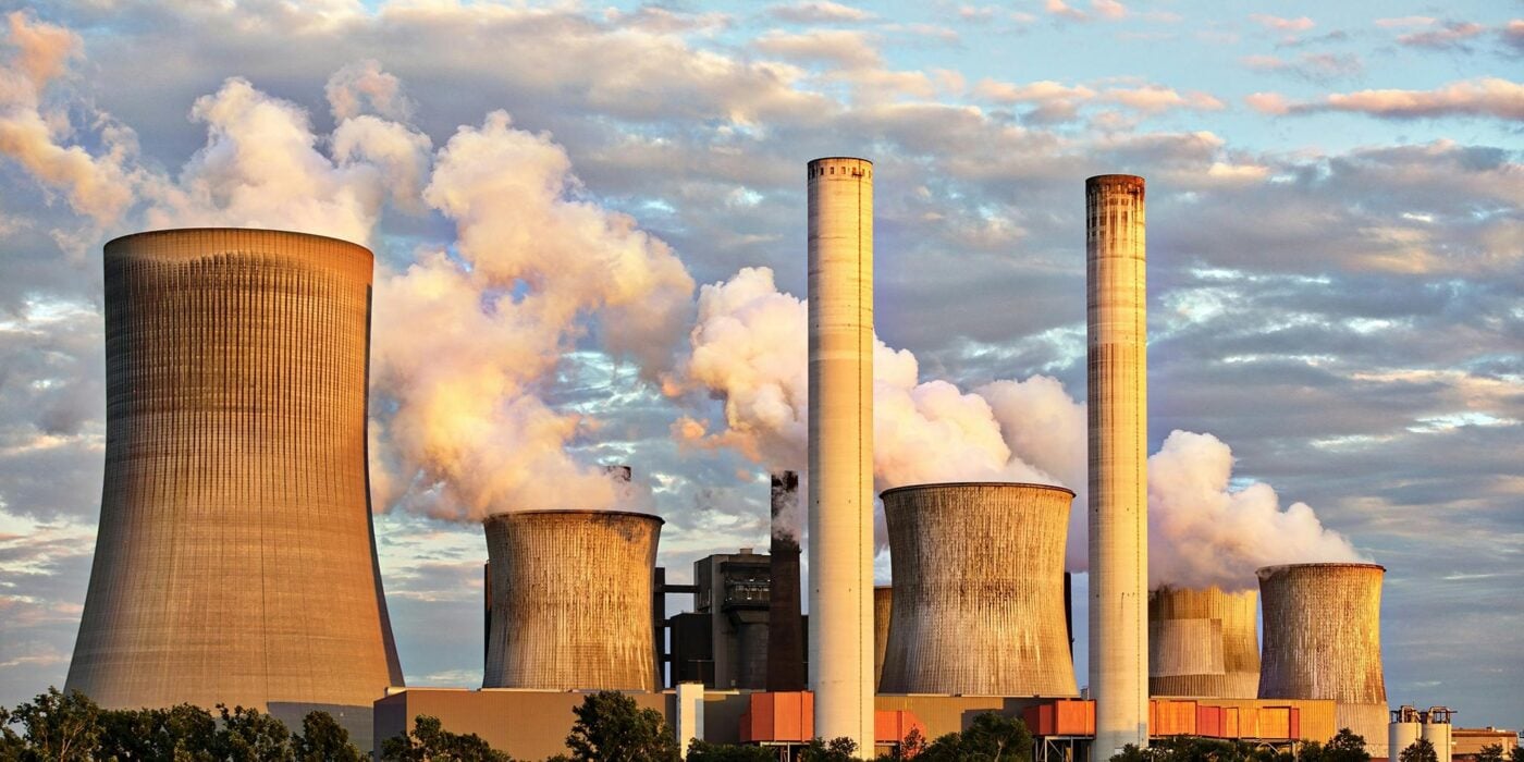 View of a power plant with smoke emissions under a cloudy sky, depicting industrial energy production.