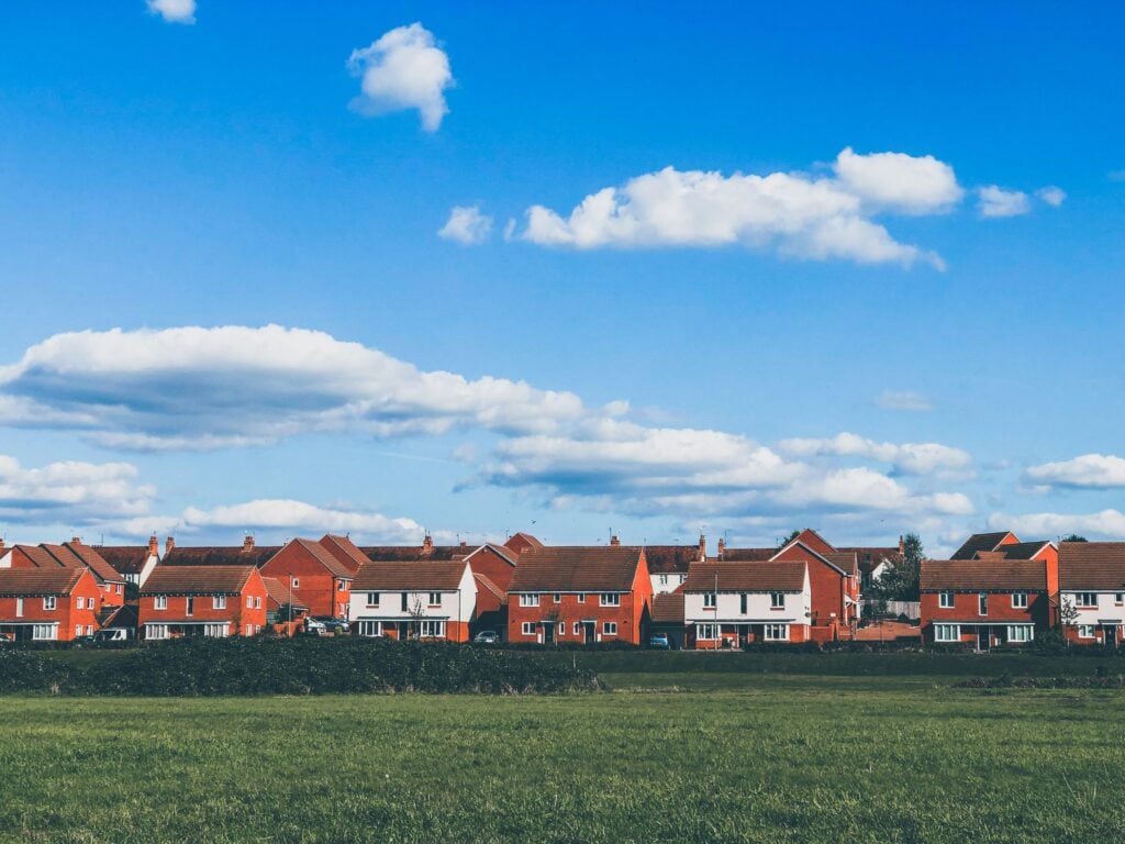A row of red brick houses with blue sky and a field in front of them.