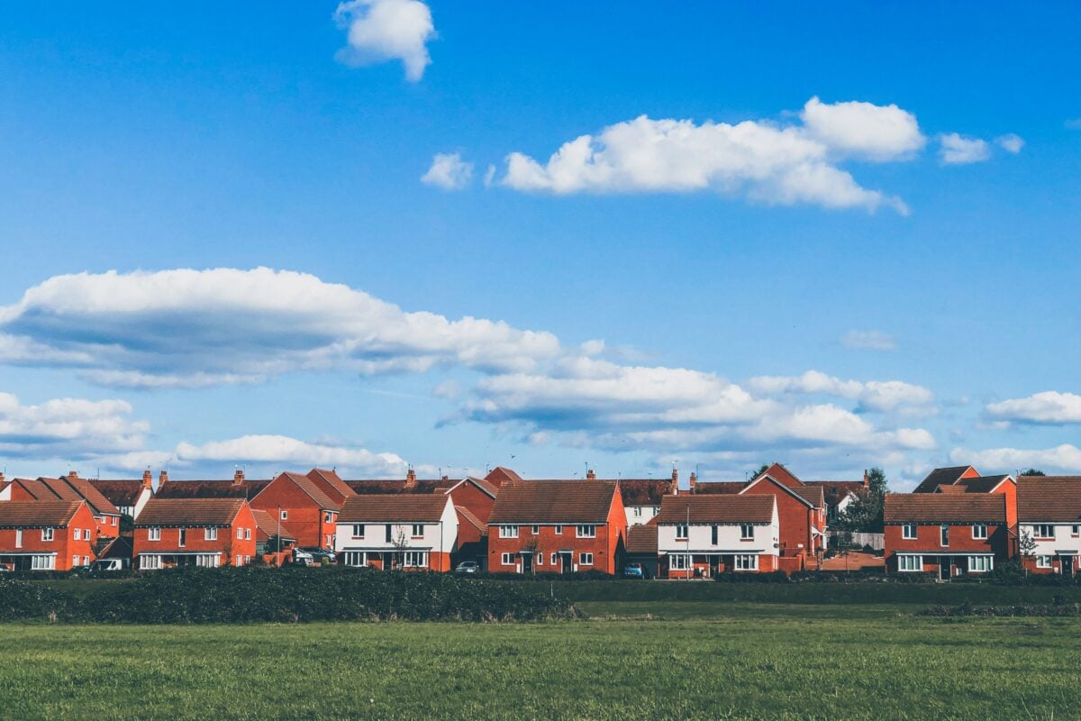 A row of red brick houses with blue sky and a field in front of them.