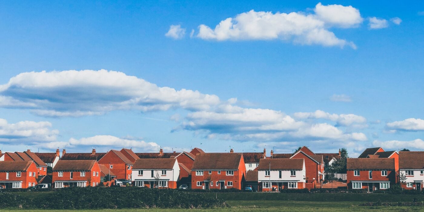 A row of red brick houses with blue sky and a field in front of them.