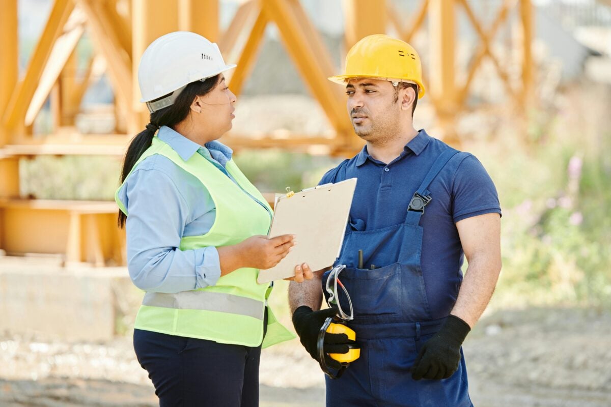 Male and female construction workers talking with safety gear at an outdoor site.