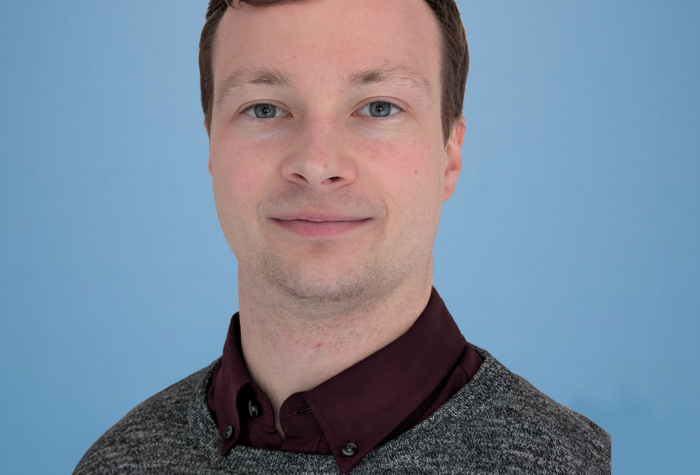 James Arber, Project Structural Engineer at Brookbanks stood in front of a blue wall