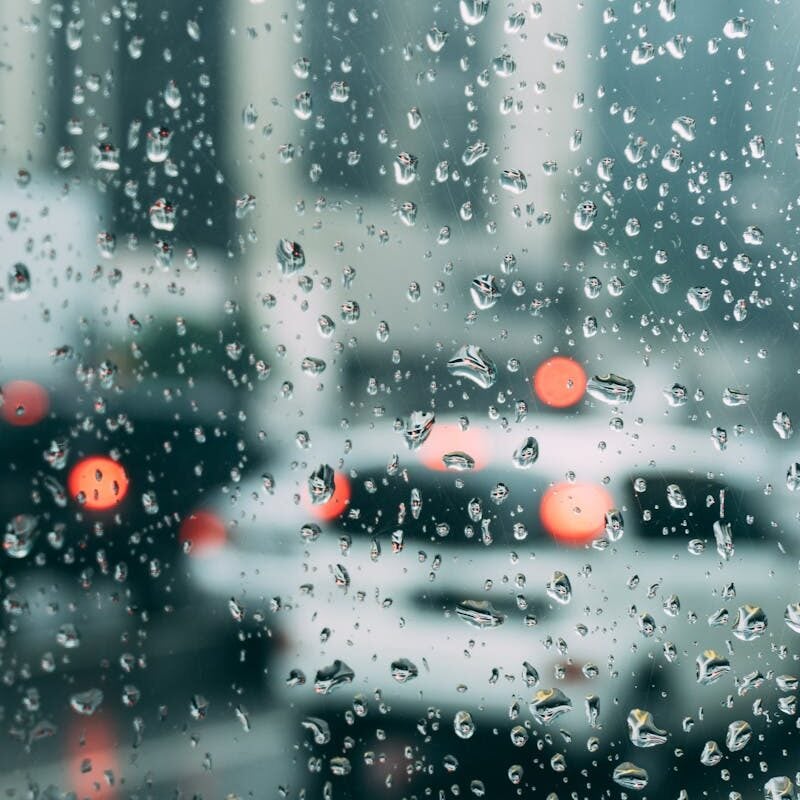 Blurred city traffic seen through a window with raindrops, a perfect rainy day scene.