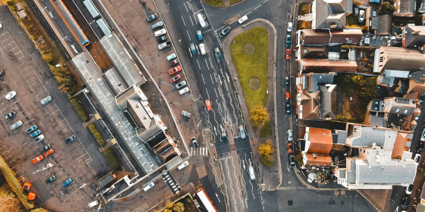 Aerial view of various vehicles driving on asphalt road near typical residential houses in suburban district on sunny day