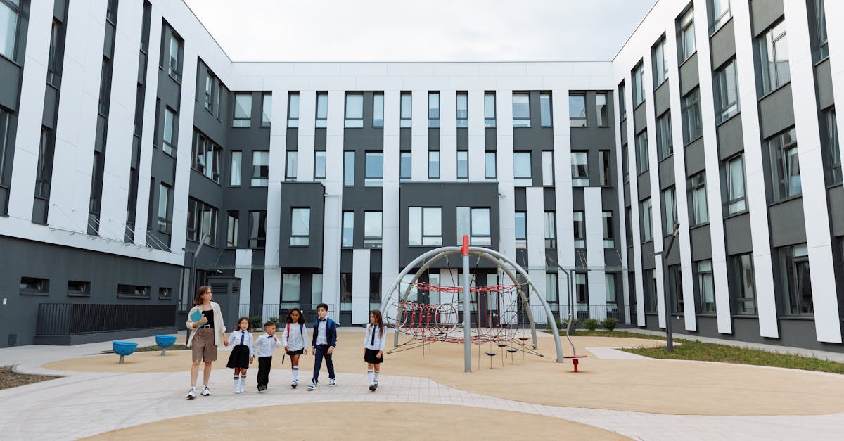 Group of students and teacher walking in a school courtyard with modern architecture and playground.