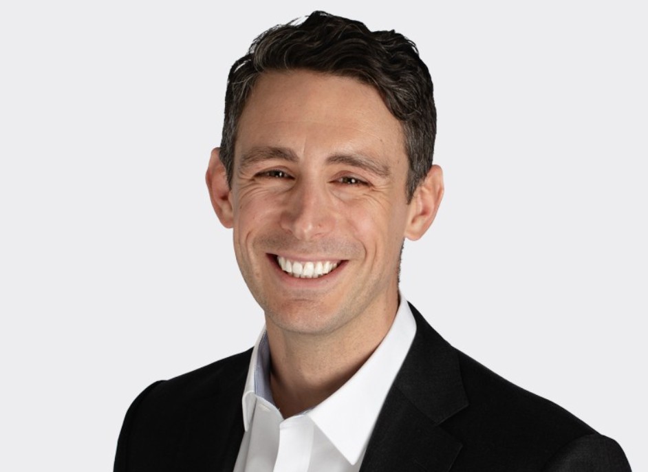 Ben Lewis a Director at CBPE Capital. He is stood in front of a white background and is smiling