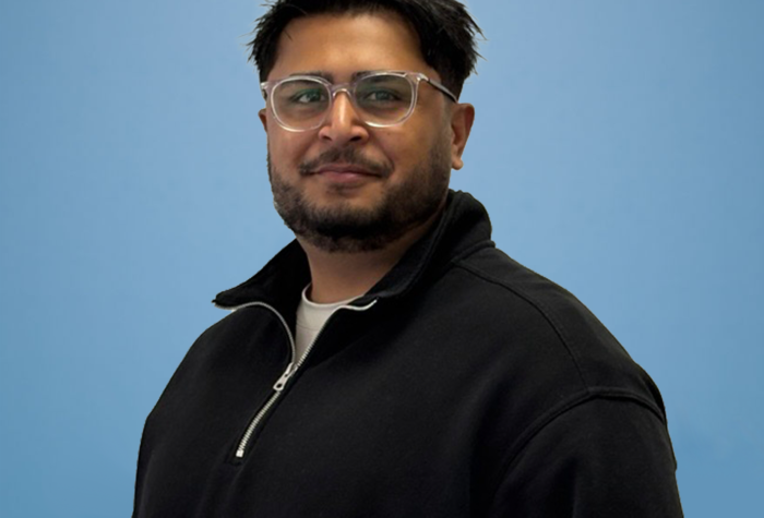Daniel Kainth a senior mechanical and electrical engineer at Brookbanks stood against a pale blue wall.
