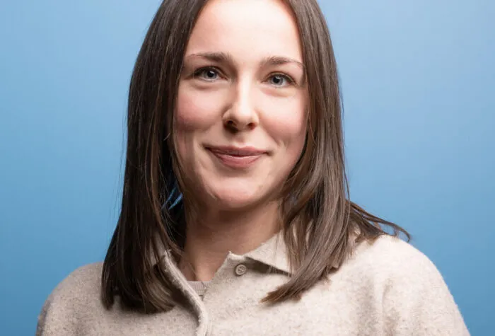 A picture of Holly Welch. A woman in her 30s with straight brown hair and brown eyes, wearing a brown jumper.