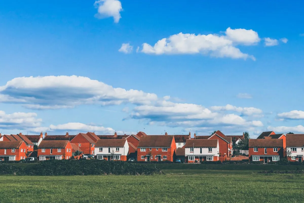A row of red brick houses with blue sky and a field in front of them.