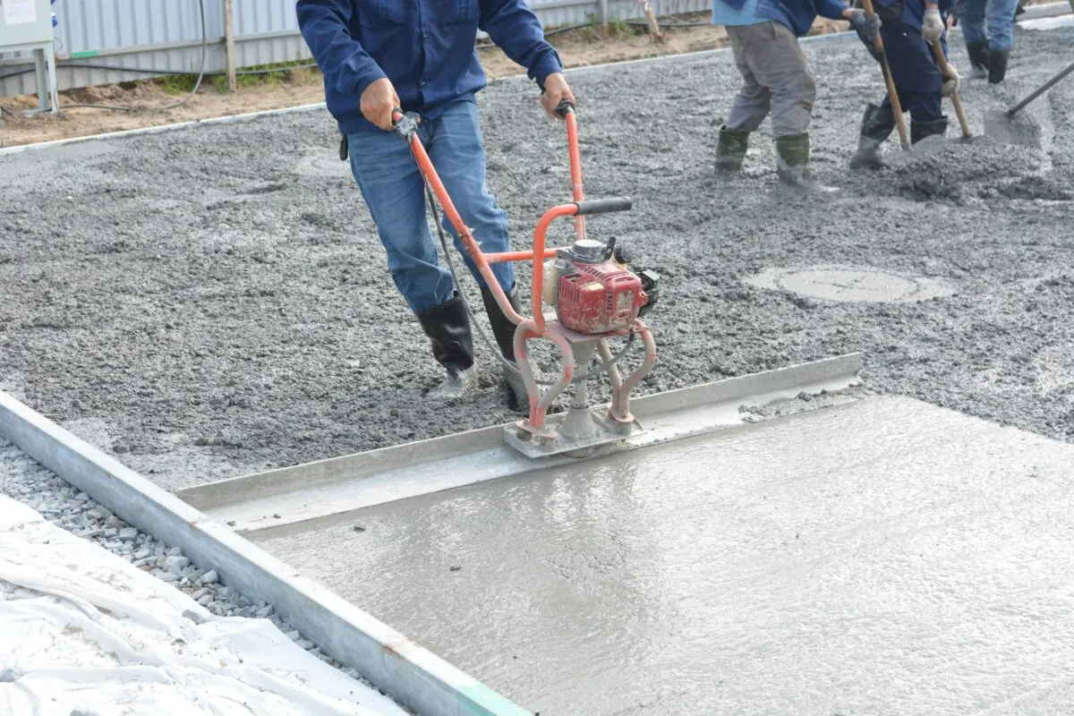 Team of construction workers using power tools to level freshly poured concrete on a building site.