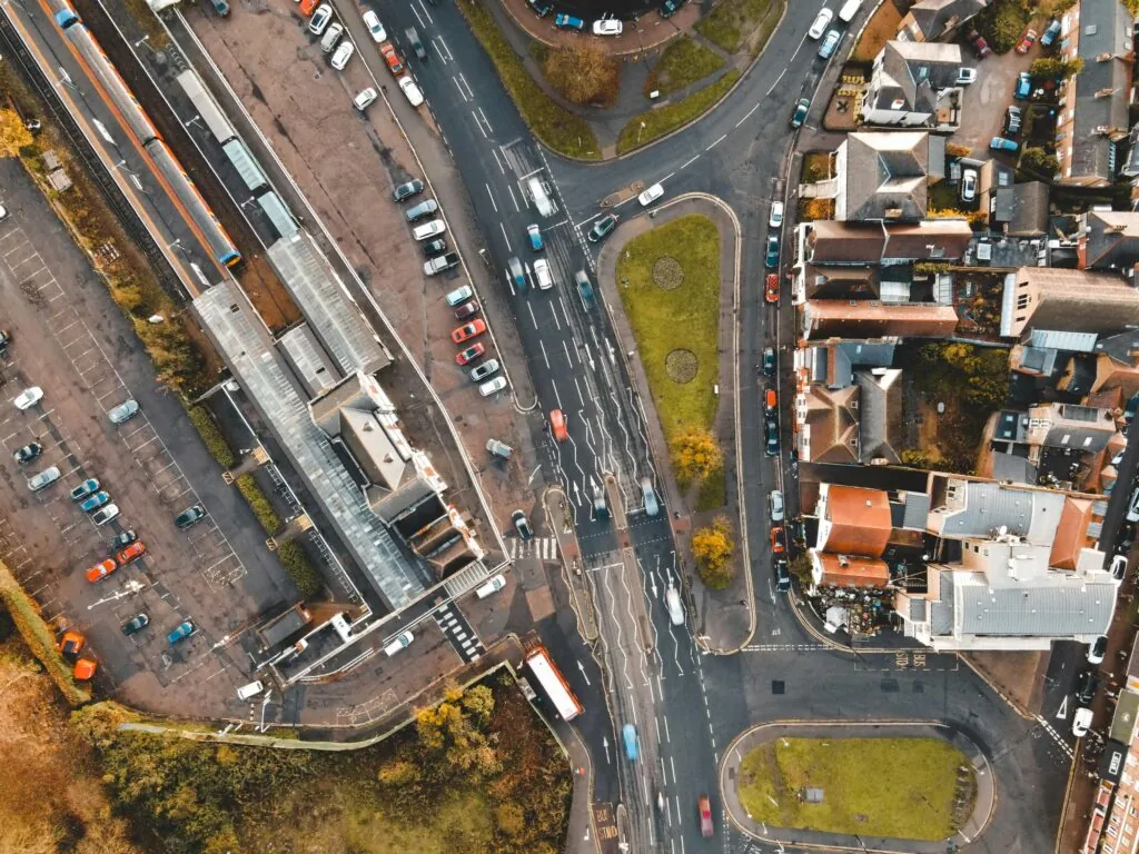 Aerial view of various vehicles driving on asphalt road near typical residential houses in suburban district on sunny day